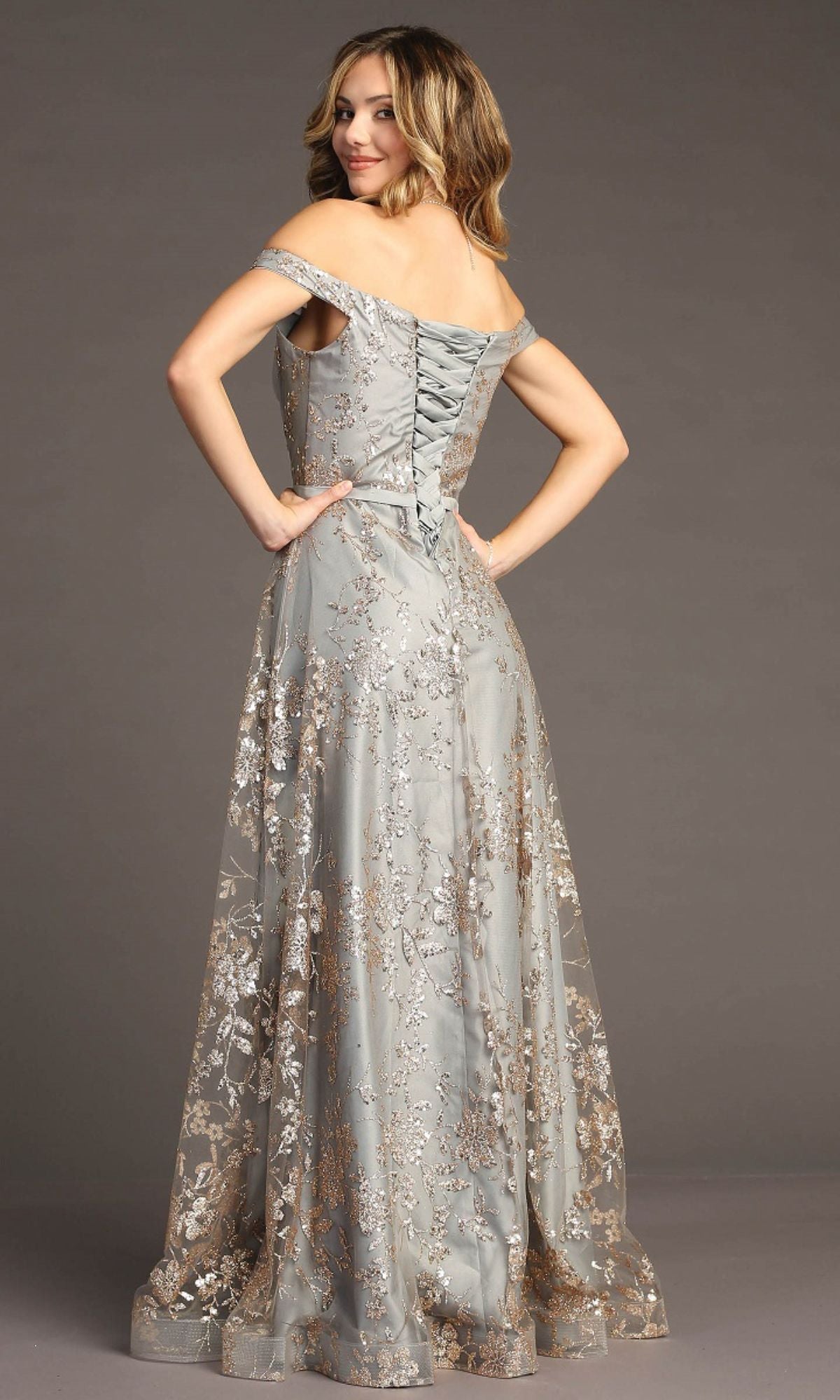 A woman stands facing away, looking over her shoulder in the stunning Glitter-Print Long Gray Prom Dress: Chicas C6533, featuring floral embroidery and a lace-up back.
